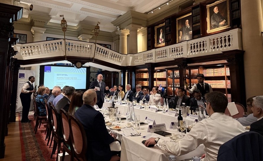 Photograph of the HFS Research and Publicis Sapient executive roundtable, held in a wood-paneled London venue. It shows roughly 20 enterprise leaders seated around a long dining table while a speaker presents from a screen at the front of the room.