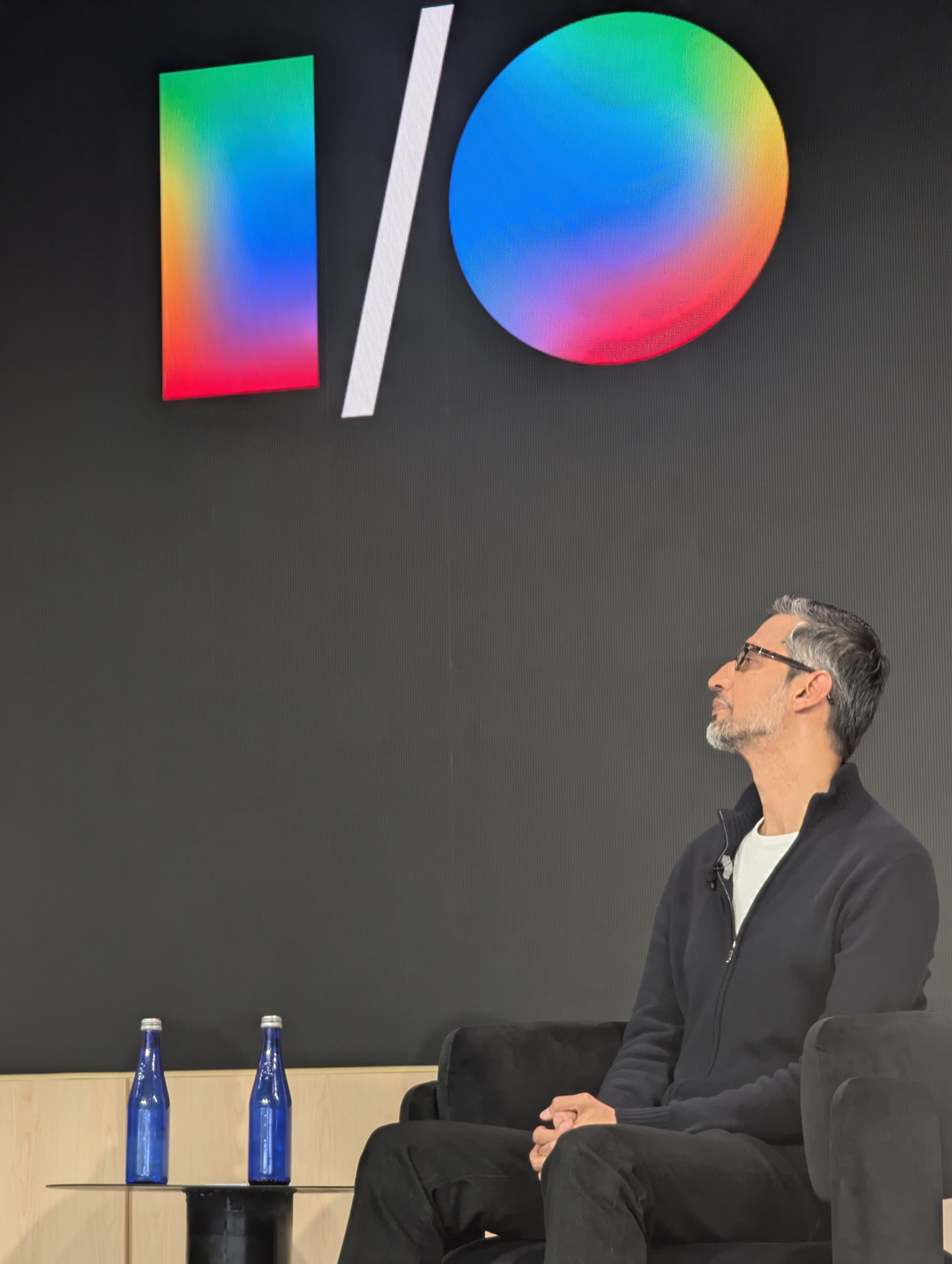 Photograph of Google CEO Sundar Pichai seated on a stage in front of a large dark backdrop displaying the Google I/O logo, used by HFS Research to illustrate analyst commentary that Pichai's I/O 2026 keynote framed enterprise AI as a question of customization and unit economics rather than raw model capability. Source: HFS Research, 2026.