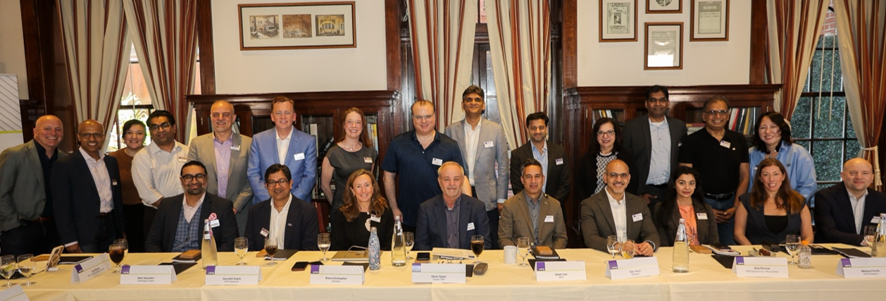 Color photograph of approximately 23 senior enterprise and HFS leaders seated and standing together at the HFS and Genpact Enterprise Debts Roundtable in a wood-paneled New York City room. No data points; decorative.